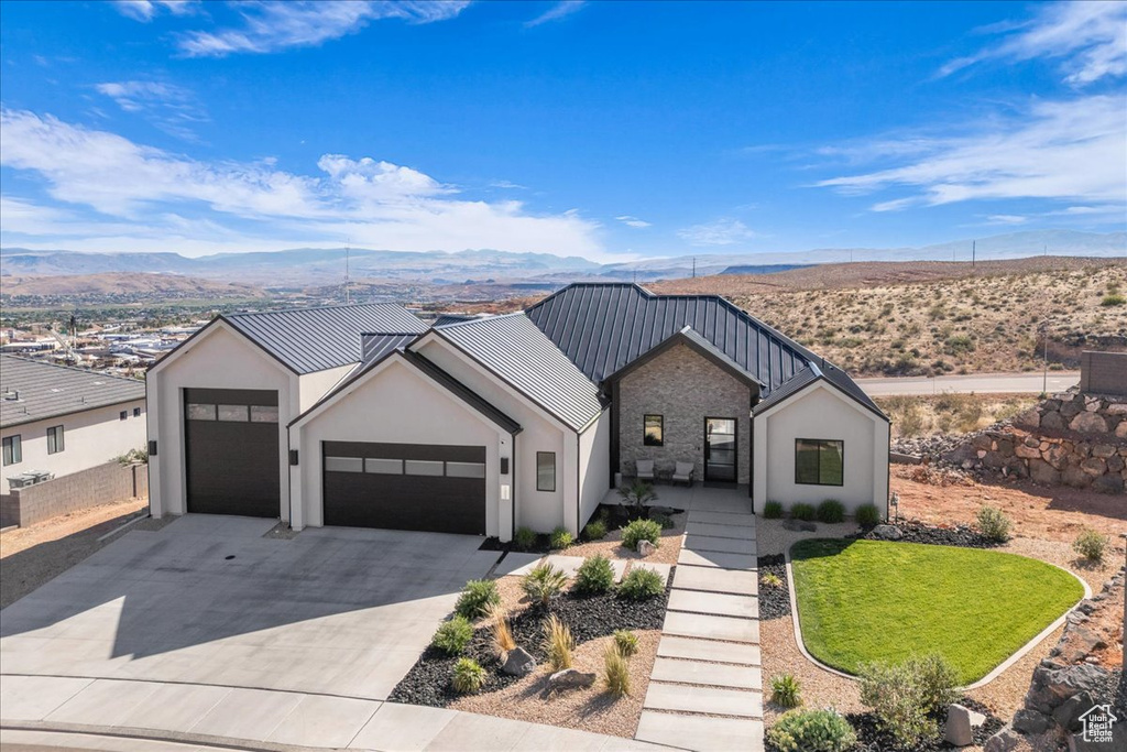 View of front of property featuring a garage, a mountain view, concrete driveway, stucco siding, and stone siding