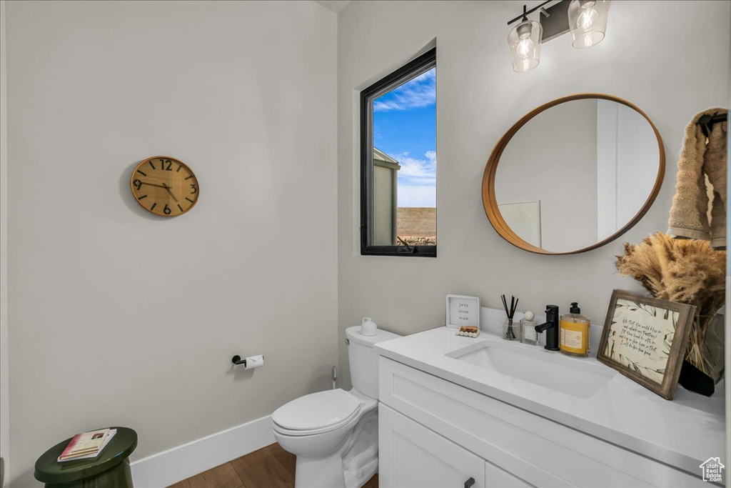 Half bath with wood finished floors, baseboards, vanity, and toilet