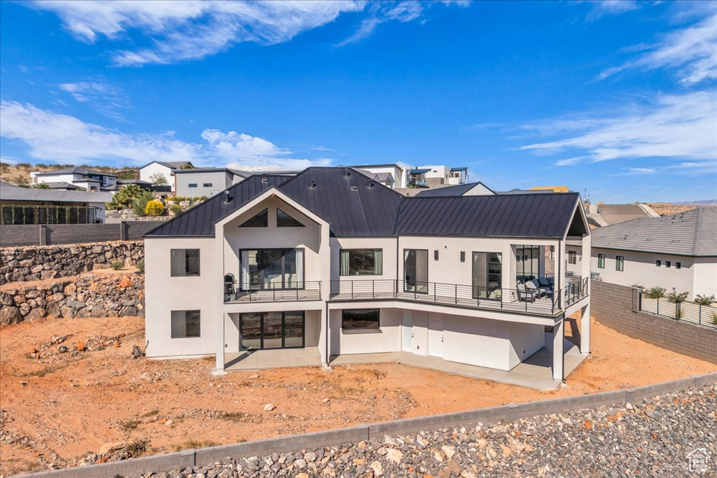 Back of property featuring a balcony, stucco siding, a patio area, metal roof, and fence