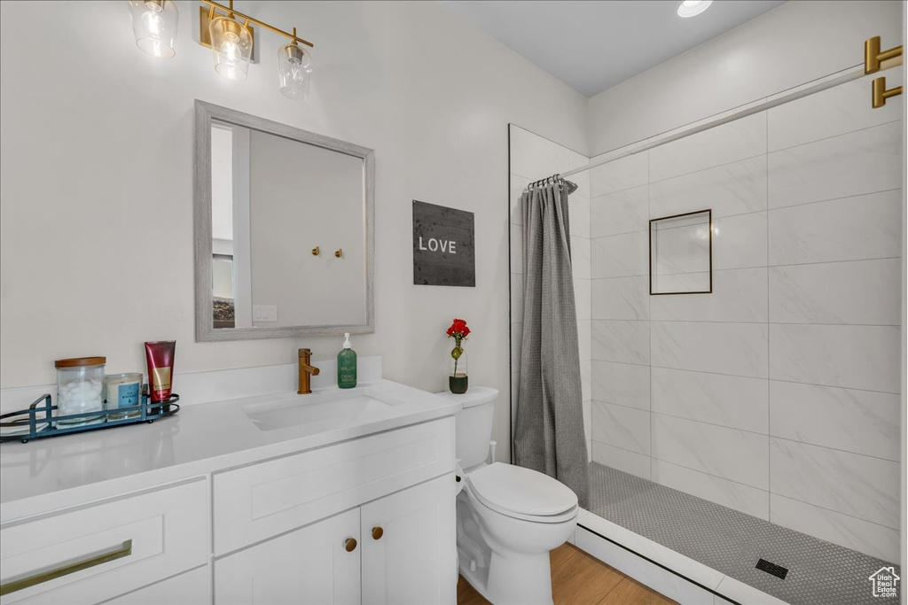 Bathroom with toilet, tiled shower, vanity, wood finished floors, and a baseboard heating unit