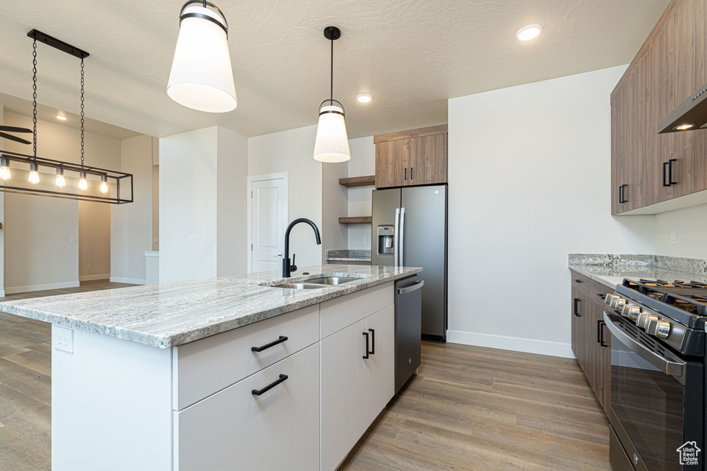 Kitchen featuring a sink, stainless steel appliances, light wood-style floors, baseboards, and a kitchen island with sink