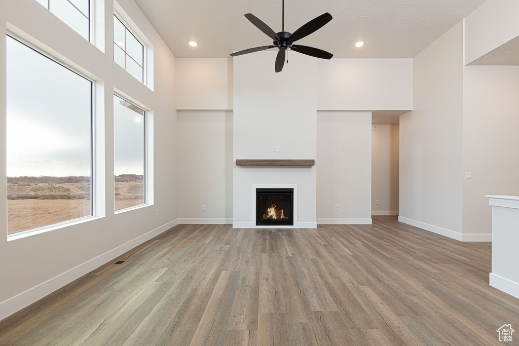 Unfurnished living room with a lit fireplace, a ceiling fan, light wood-style flooring, baseboards, and recessed lighting