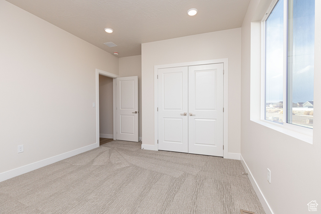 Unfurnished bedroom featuring light carpet, a closet, baseboards, and recessed lighting