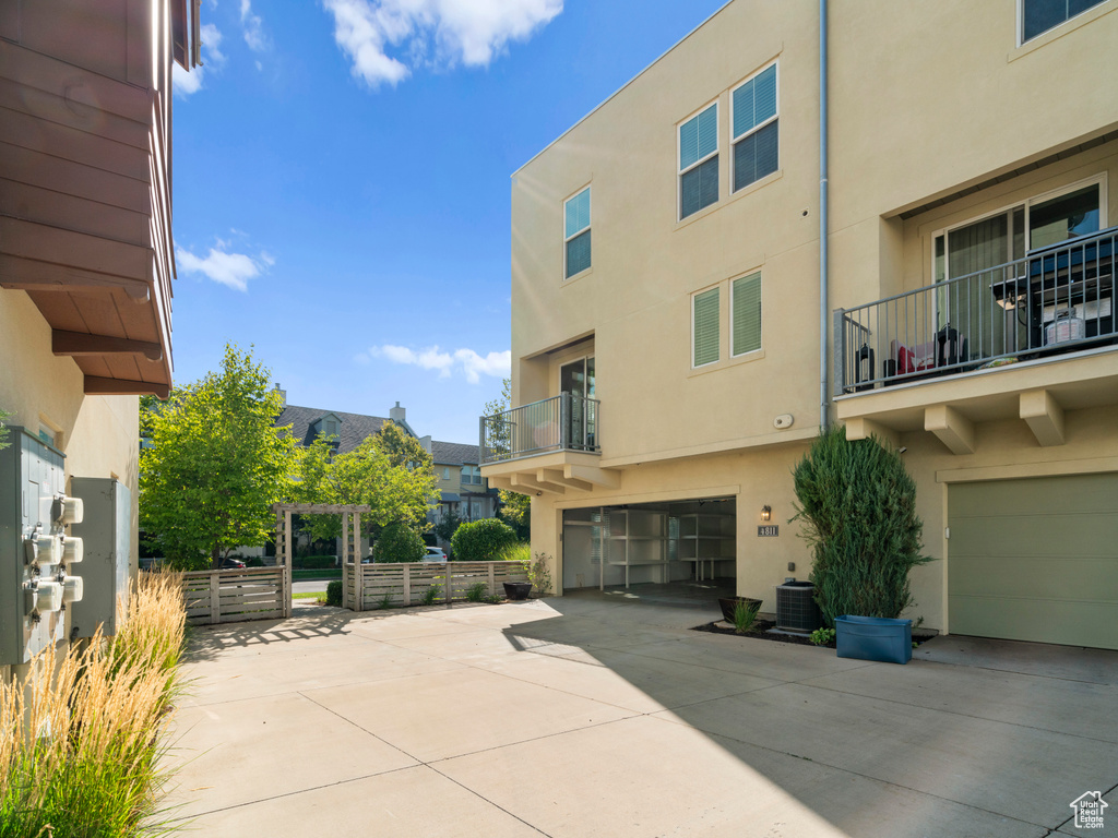 View of patio with driveway, an attached garage, a balcony, and central AC