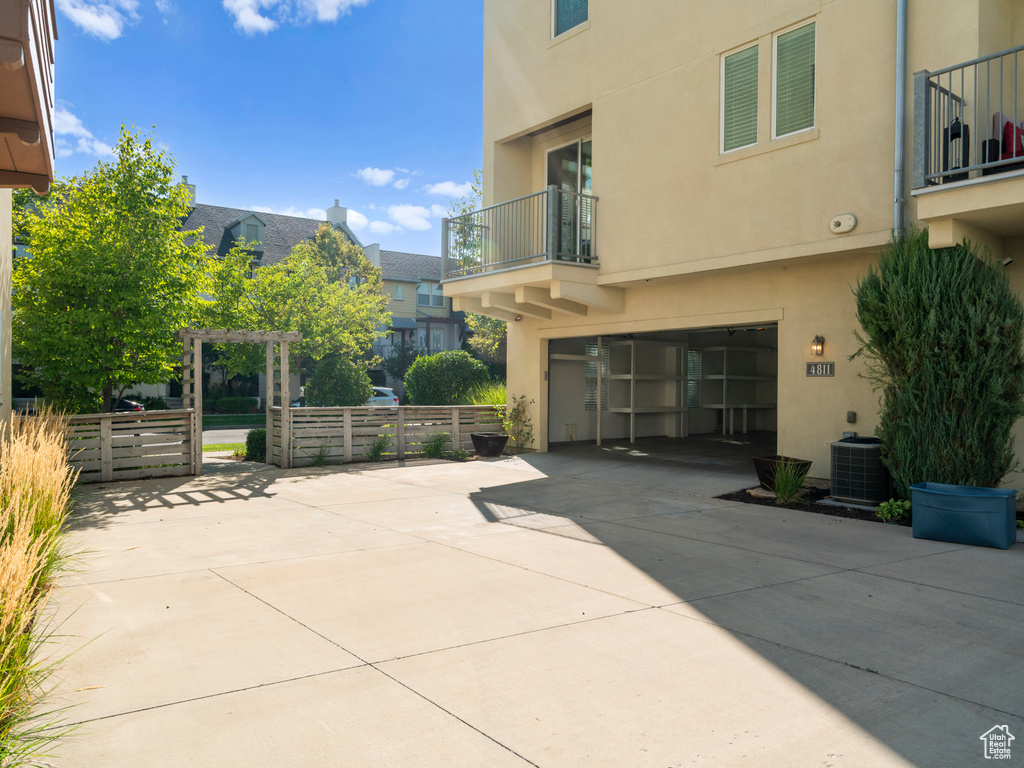 View of patio featuring a balcony, concrete driveway, fence, a garage, and central air condition unit