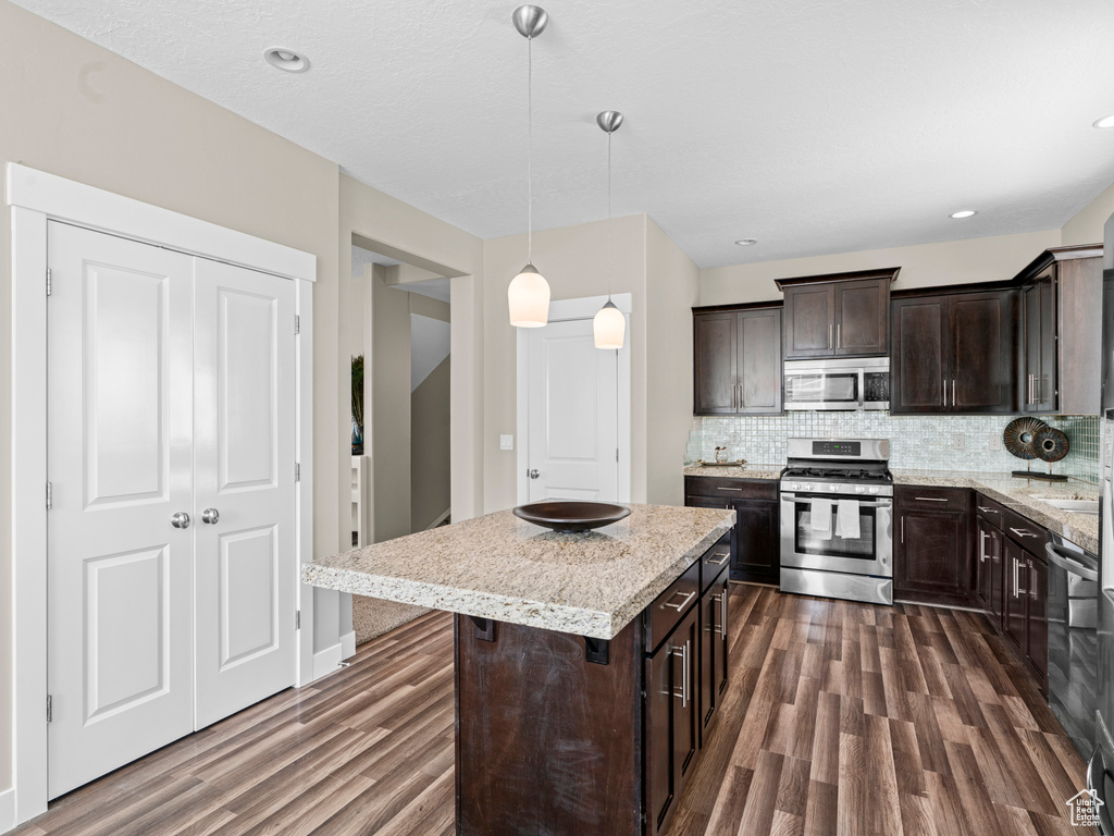 Kitchen with stainless steel appliances, dark wood-style floors, dark brown cabinets, backsplash, and a center island
