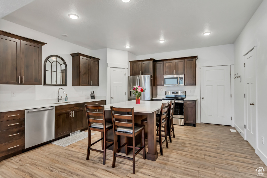 Kitchen with stainless steel appliances, a sink, a kitchen breakfast bar, dark brown cabinets, and a kitchen island