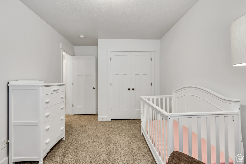 Bedroom with light colored carpet, a closet, and a nursery area
