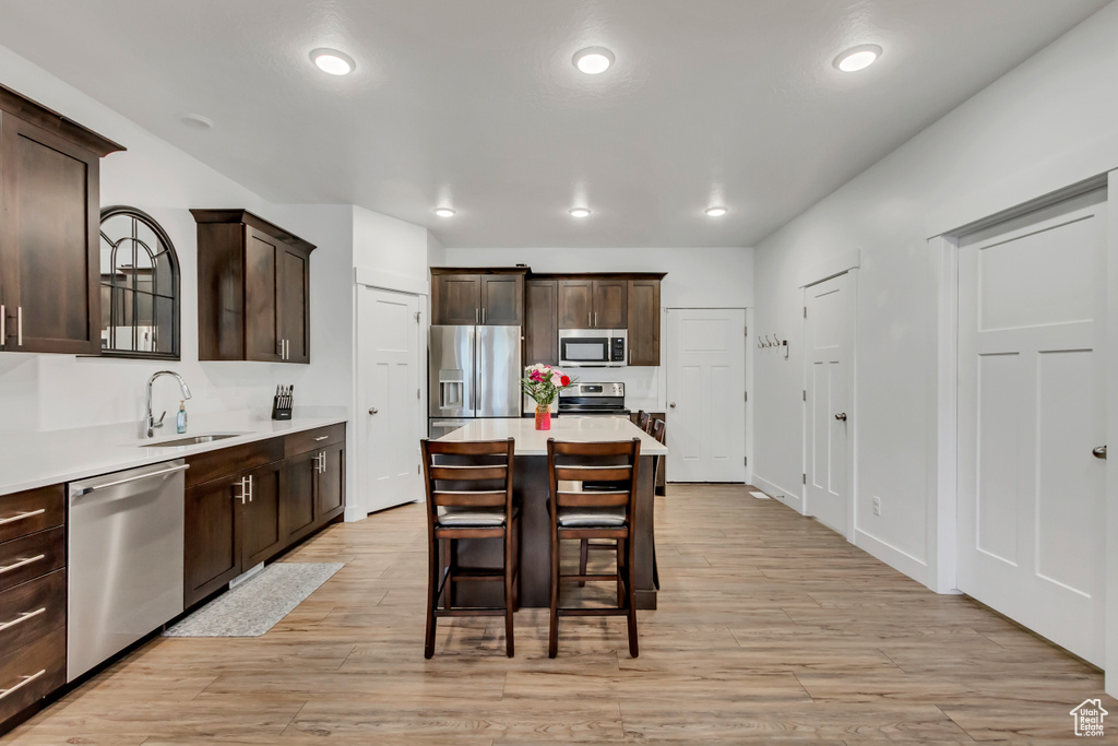 Kitchen with appliances with stainless steel finishes, a sink, dark brown cabinets, light countertops, and recessed lighting