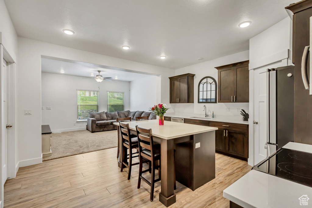 Kitchen featuring a sink, dark brown cabinets, a ceiling fan, light countertops, and a breakfast bar area