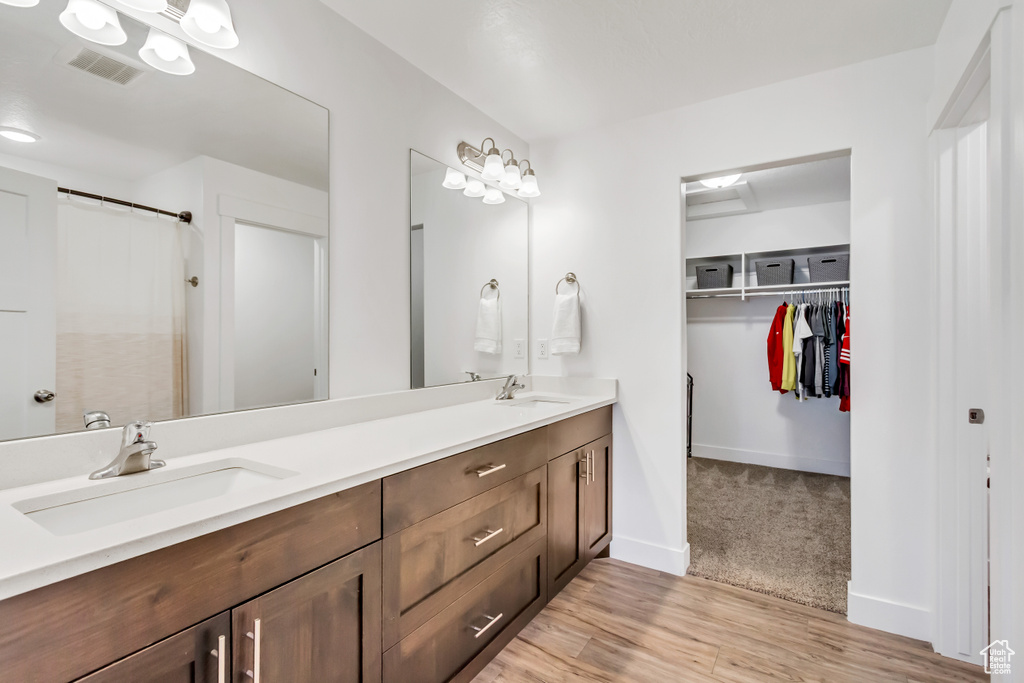 Bathroom with double vanity, wood finished floors, a walk in closet, curtained shower, and baseboards