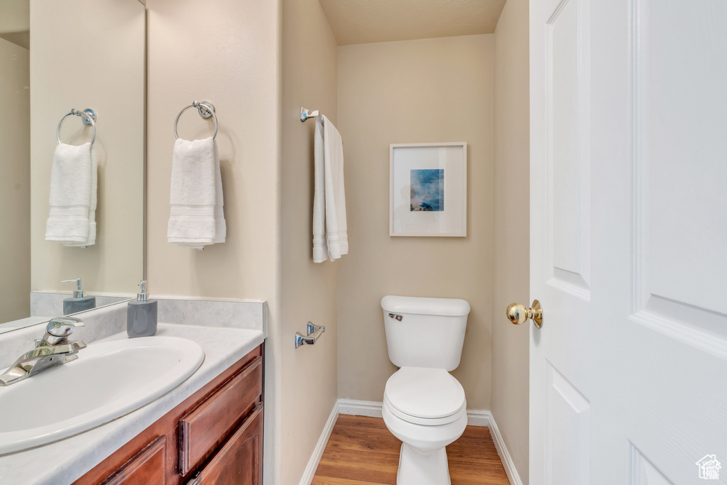 Half bath featuring wood finished floors, toilet, vanity, and baseboards