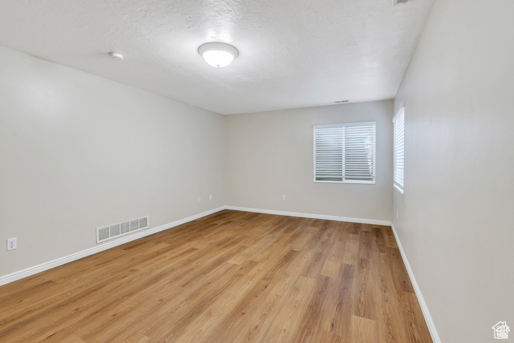 Empty room with baseboards, light wood-style floors, a smoke detector, and a textured ceiling