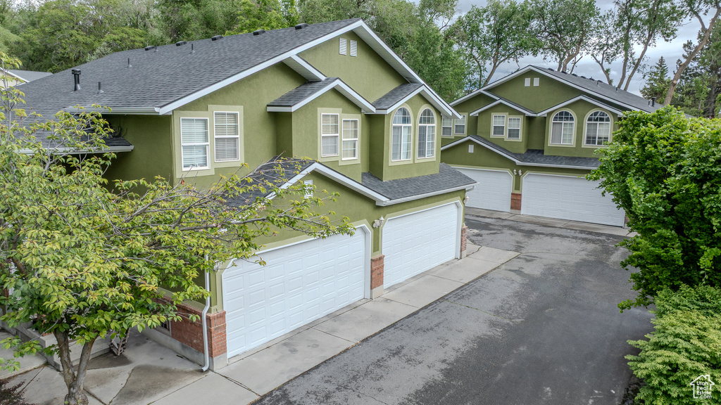 View of front facade featuring a shingled roof, stucco siding, asphalt driveway, a garage, and brick siding