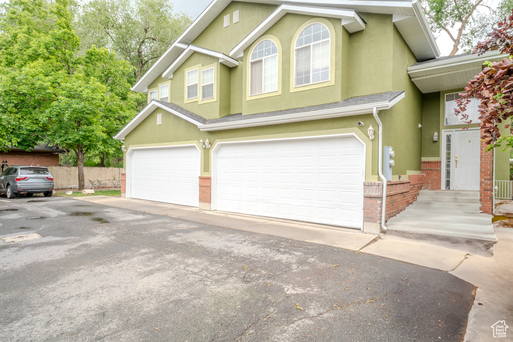 View of front of home featuring stucco siding, a garage, asphalt driveway, brick siding, and fence