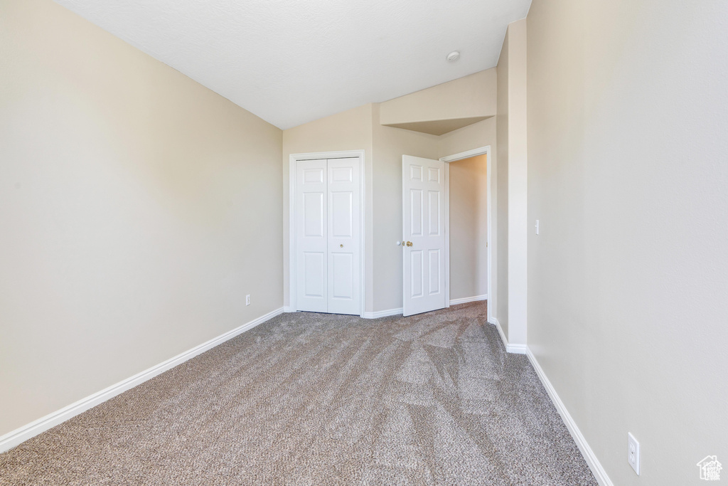 Unfurnished bedroom with carpet floors, lofted ceiling, baseboards, and a closet