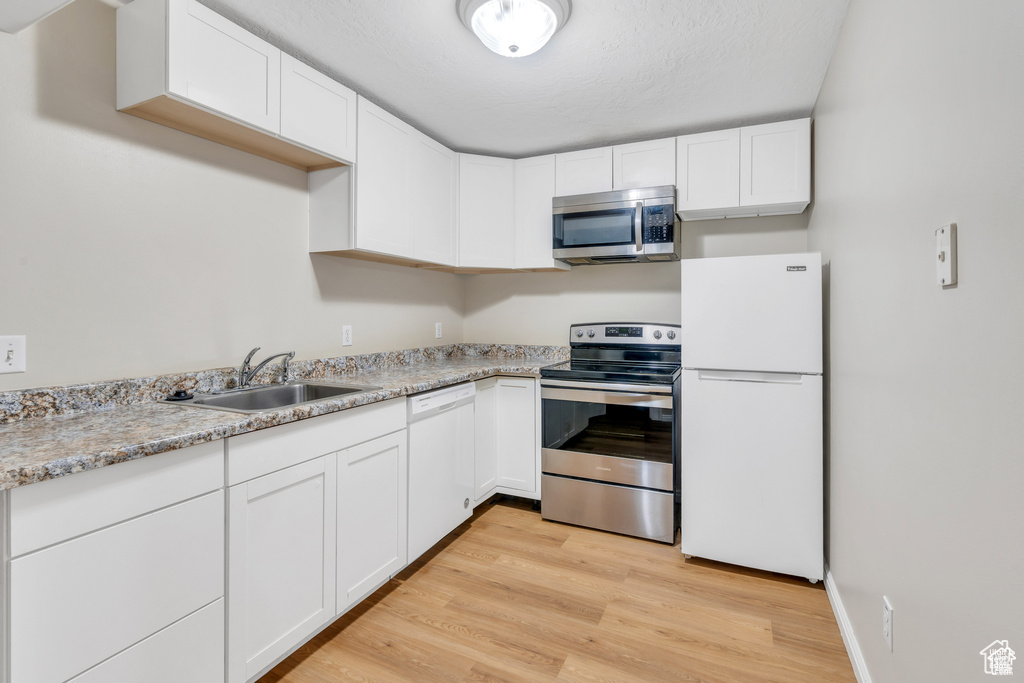 Kitchen with appliances with stainless steel finishes, a sink, white cabinetry, light wood-style flooring, and light countertops