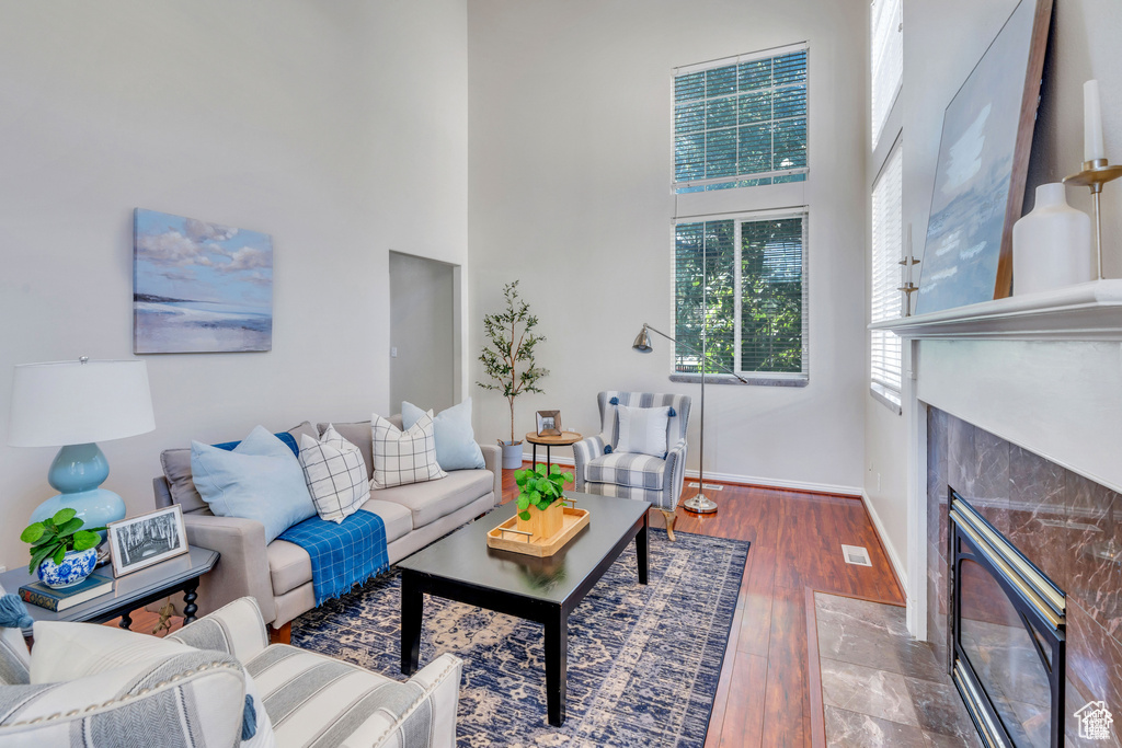 Living area featuring a premium fireplace, a towering ceiling, baseboards, and wood finished floors