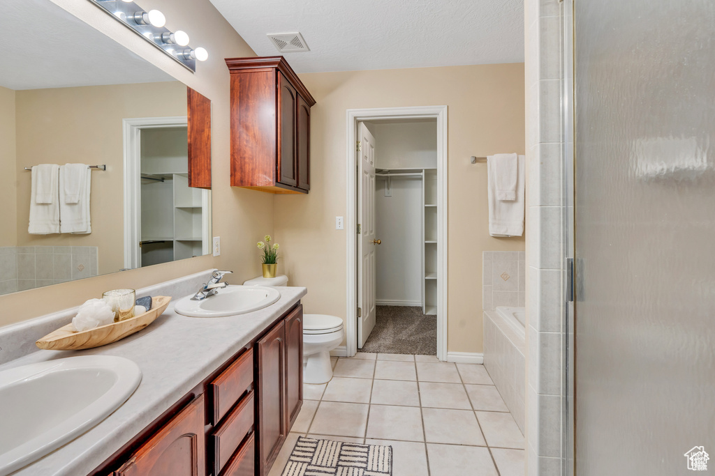 Bathroom featuring tile patterned floors, a walk in closet, toilet, and double vanity
