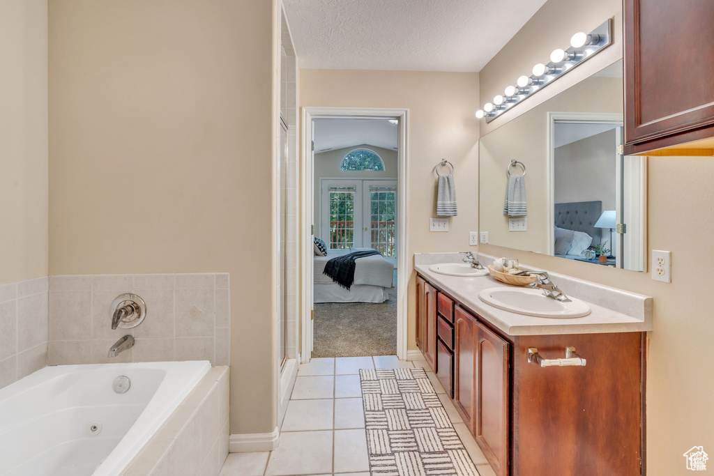Ensuite bathroom with double vanity, a tub with jets, tile patterned floors, french doors, and a textured ceiling