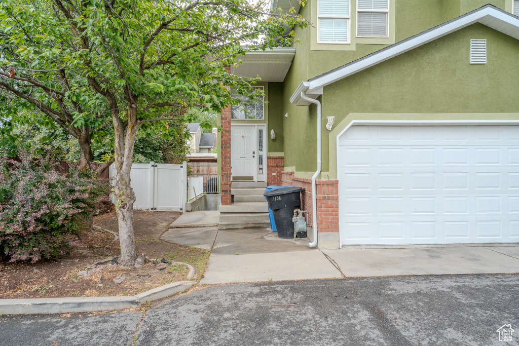 View of front of property with stucco siding, a garage, driveway, fence, and brick siding