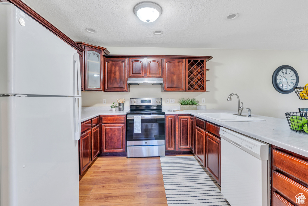 Kitchen with white appliances, a sink, dark brown cabinets, under cabinet range hood, and light countertops