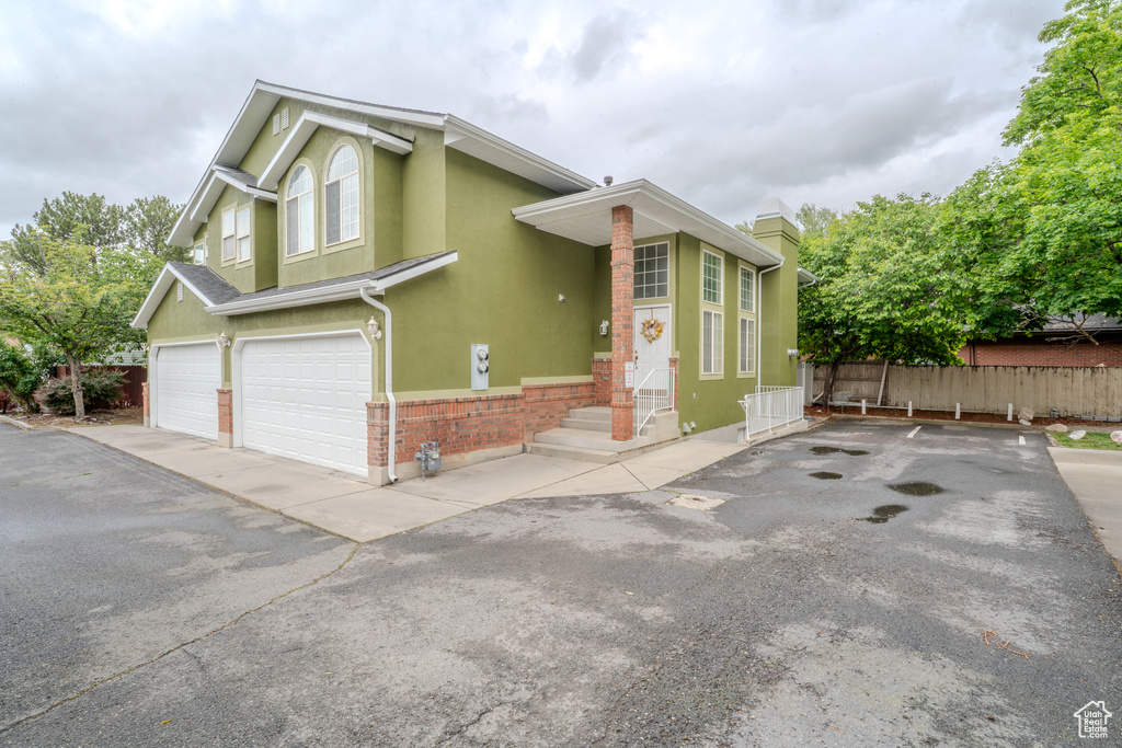 View of front of house with a garage, driveway, fence, brick siding, and stucco siding