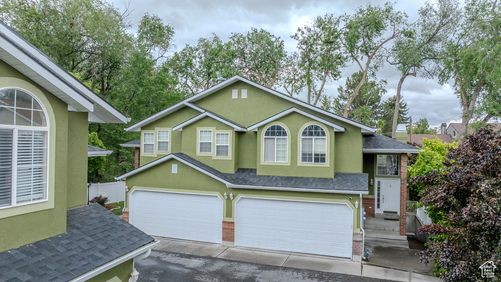 Traditional-style house with roof with shingles, an attached garage, stucco siding, brick siding, and fence