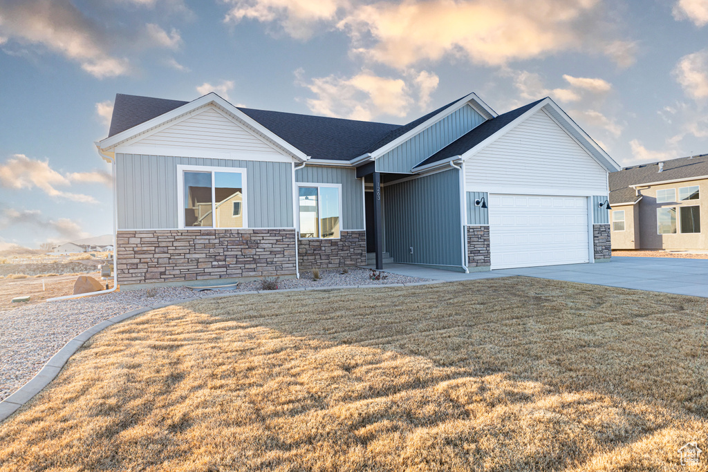 View of front of house featuring stone siding, an attached garage, a front lawn, and board and batten siding