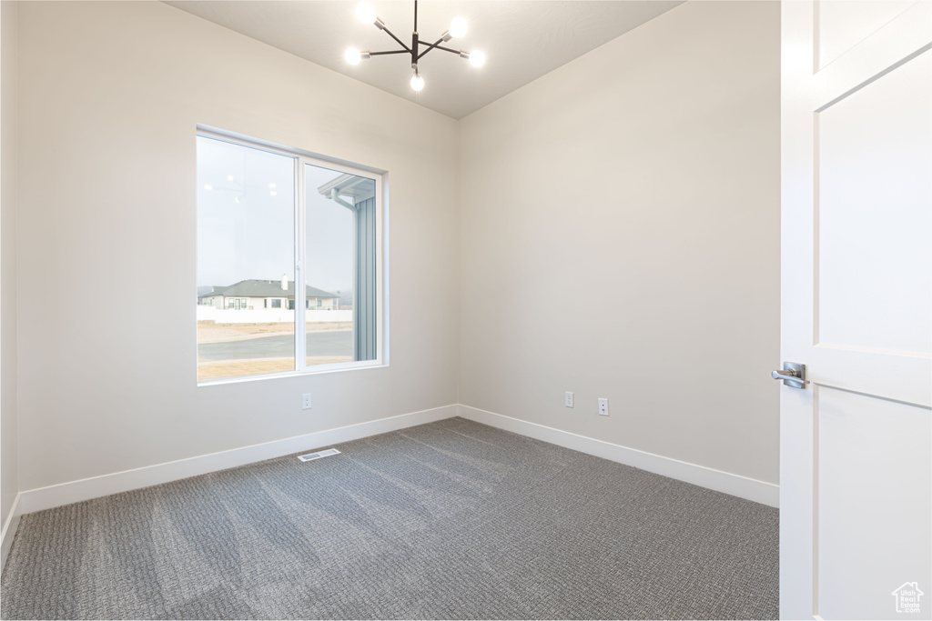 Carpeted empty room with a chandelier and baseboards