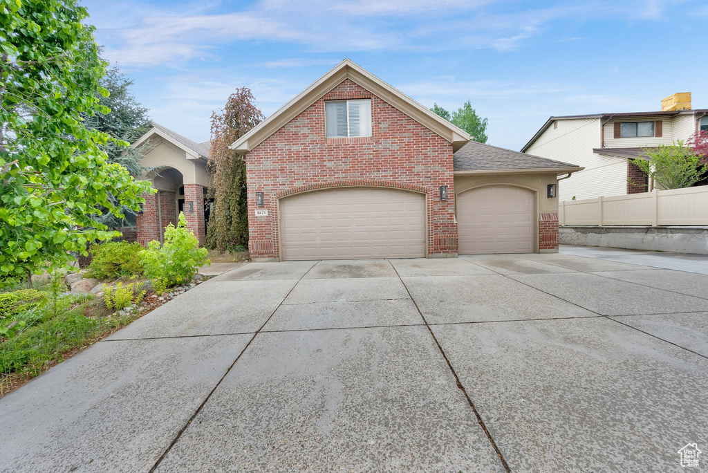 Traditional-style home featuring brick siding, driveway, fence, a shingled roof, and an attached garage