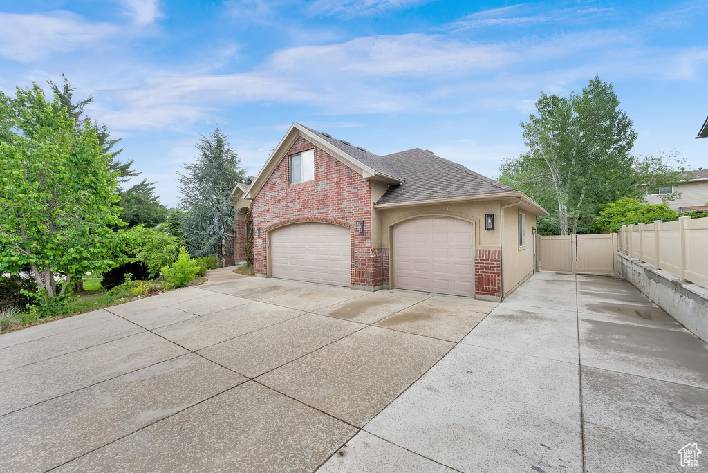 View of side of home featuring driveway, fence, a shingled roof, brick siding, and an attached garage