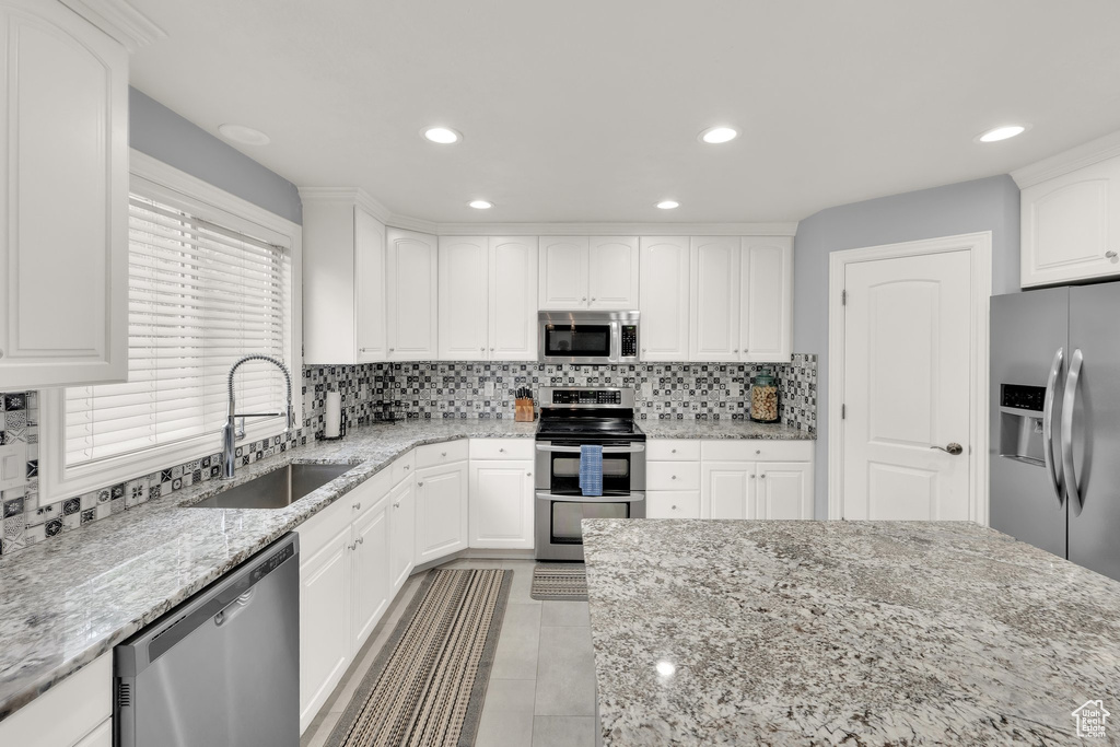 Kitchen with appliances with stainless steel finishes, a sink, backsplash, light stone counters, and white cabinetry