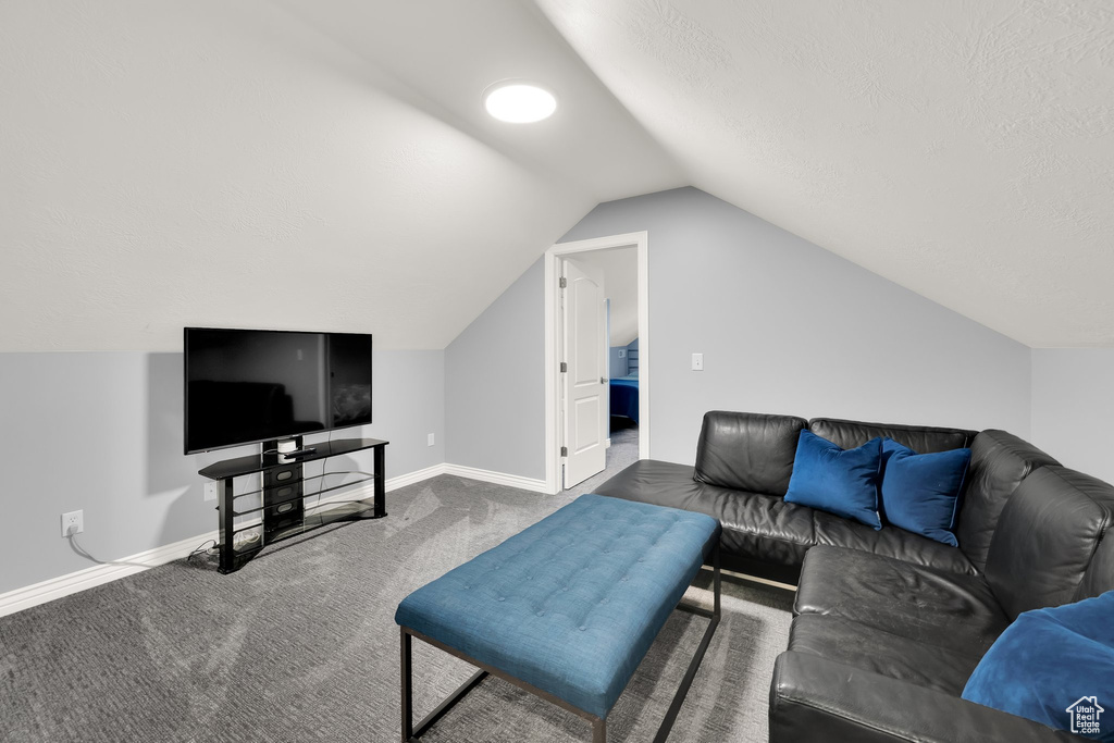 Living room with vaulted ceiling, carpet floors, baseboards, and a textured ceiling