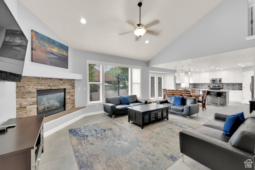 Living area featuring ceiling fan, high vaulted ceiling, a stone fireplace, and recessed lighting