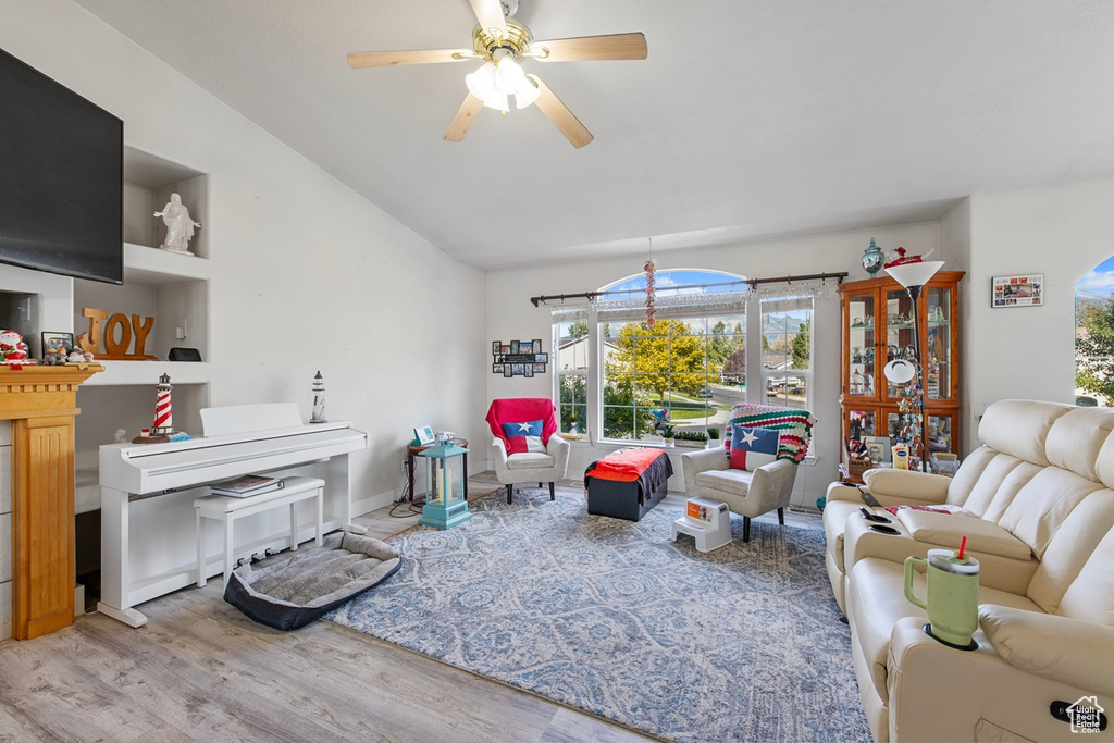 Living room with wood finished floors, a ceiling fan, lofted ceiling, and baseboards