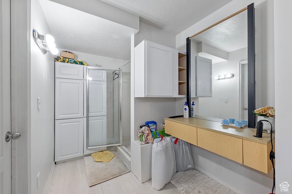 Full bathroom featuring a stall shower, a textured ceiling, vanity, baseboards, and wood finished floors