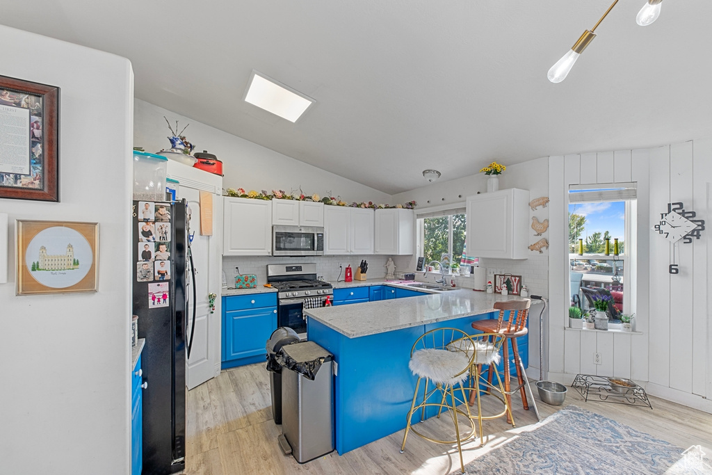 Kitchen featuring stainless steel appliances, light wood-style flooring, blue cabinetry, a peninsula, and vaulted ceiling