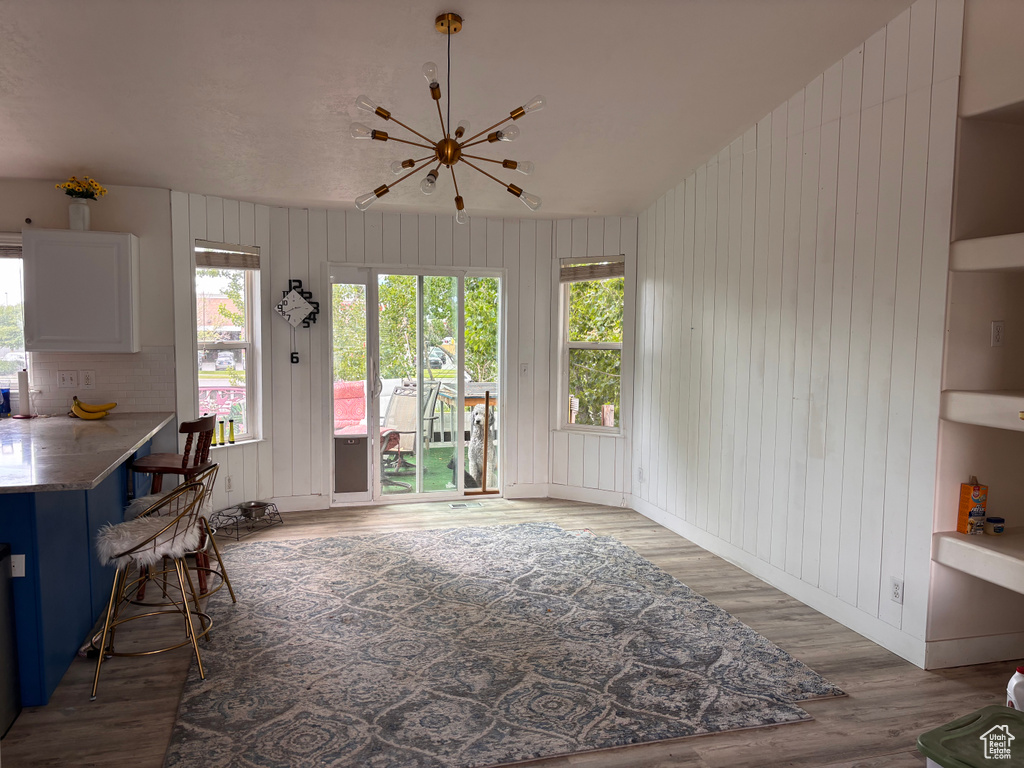 Dining area featuring wood finished floors, healthy amount of natural light, a chandelier, wood walls, and baseboards
