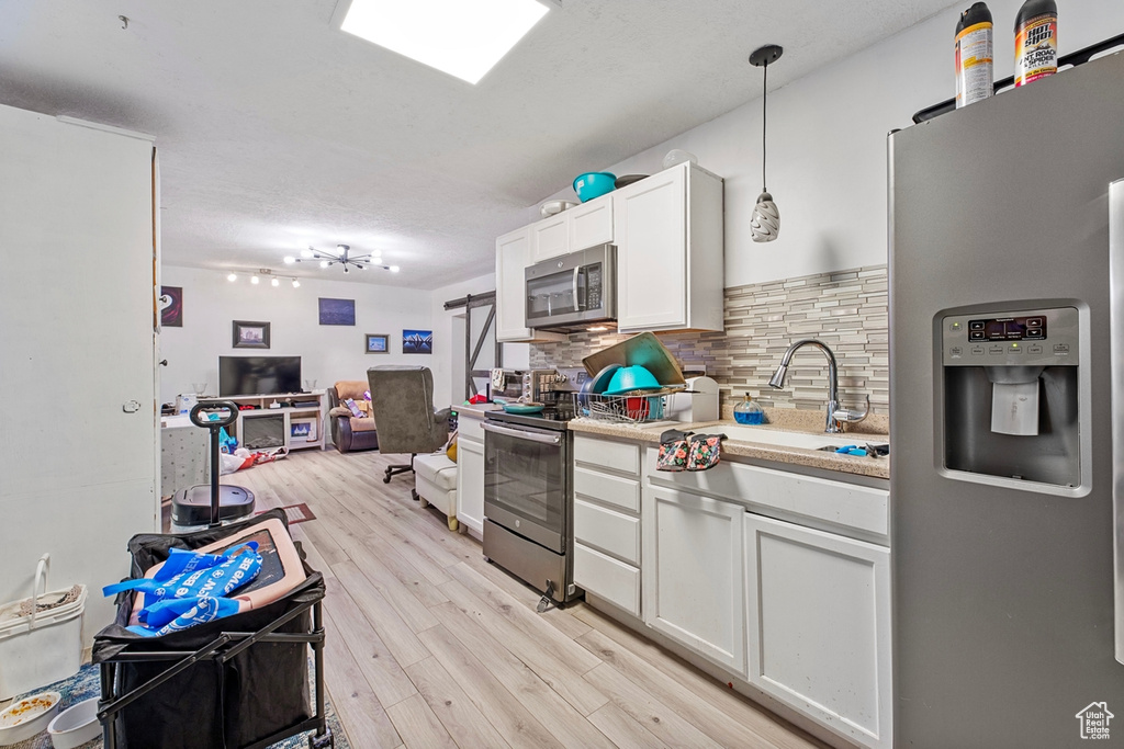 Kitchen featuring stainless steel appliances, light wood-style flooring, a sink, decorative backsplash, and light countertops