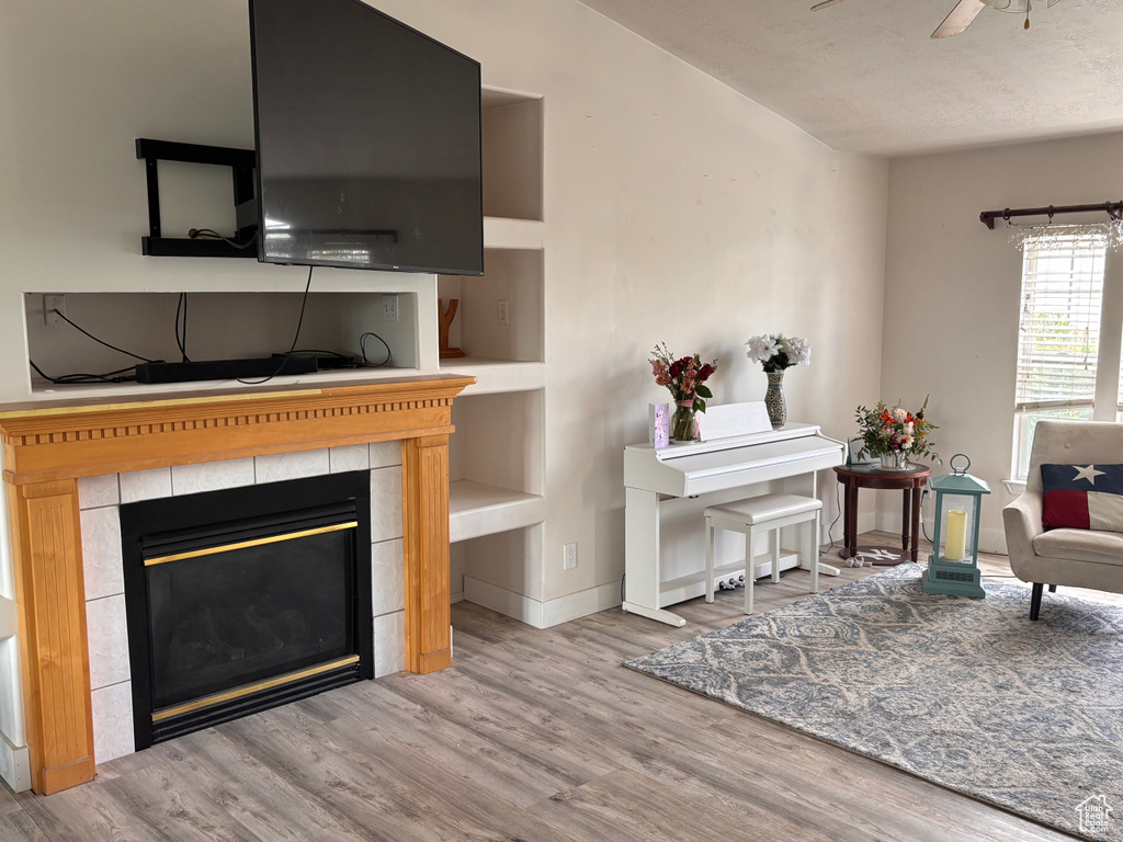Living room with wood finished floors, a tile fireplace, ceiling fan, and baseboards