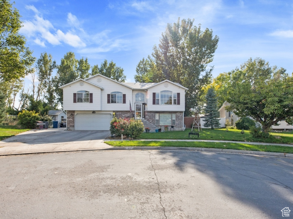 Split foyer home featuring brick siding, an attached garage, driveway, and a front yard