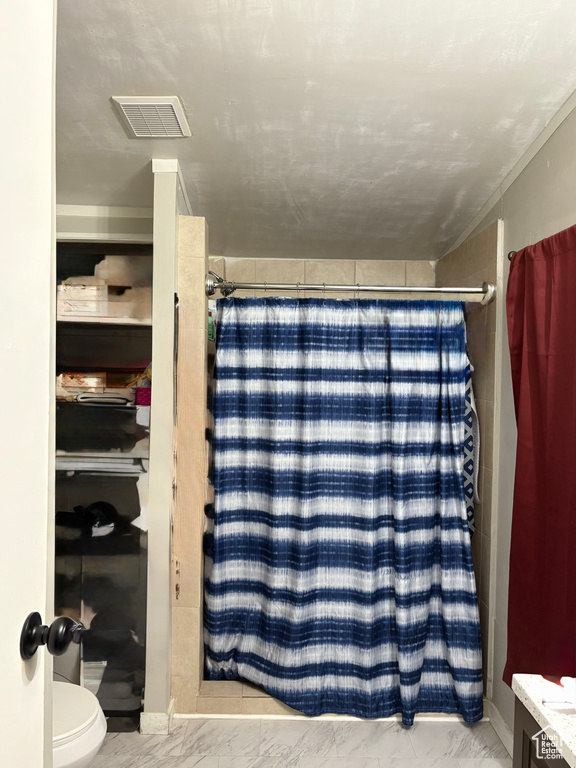 Bathroom with marble finish floors, a shower with curtain, and toilet