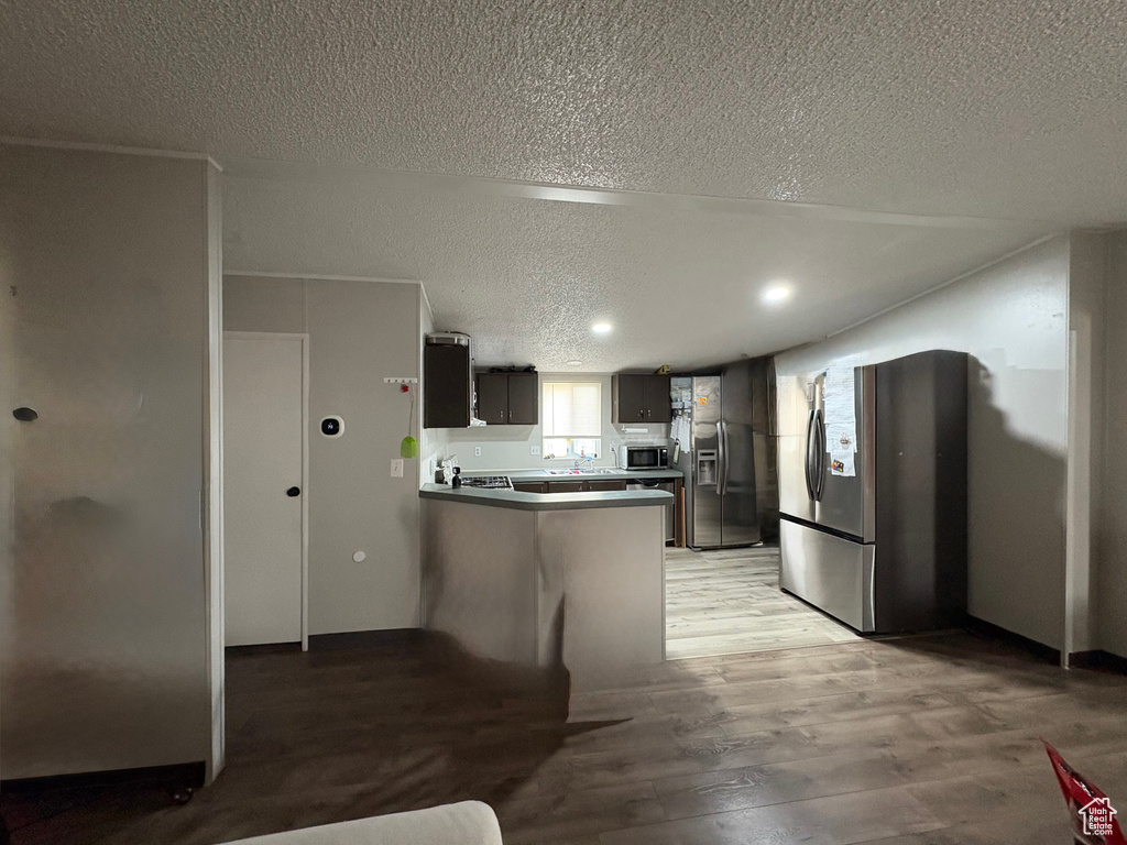 Kitchen featuring appliances with stainless steel finishes, a textured ceiling, a peninsula, light wood-type flooring, and recessed lighting