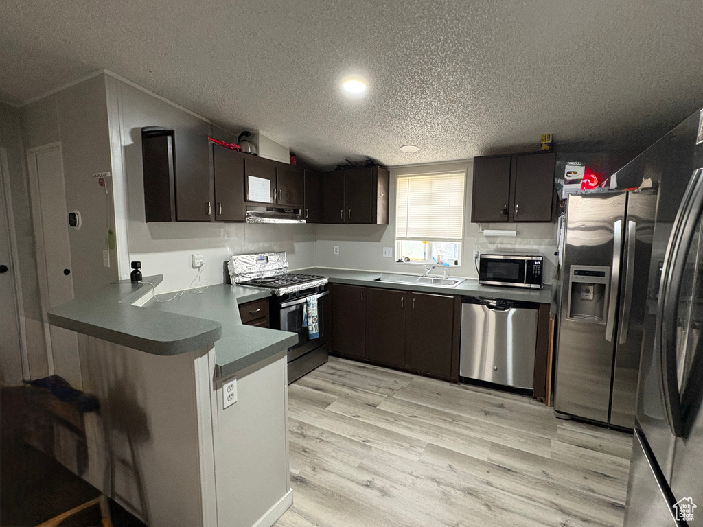 Kitchen featuring stainless steel appliances, a textured ceiling, a sink, a peninsula, and under cabinet range hood