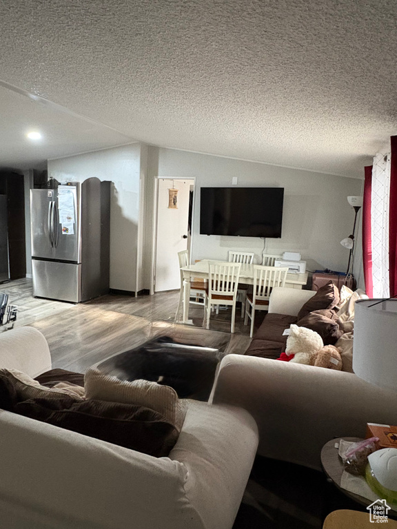 Living area with a textured ceiling, wood finished floors, vaulted ceiling, and recessed lighting