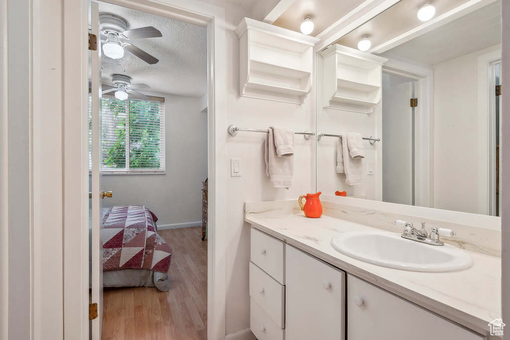 Bathroom with wood finished floors, vanity, baseboards, a ceiling fan, and a textured ceiling