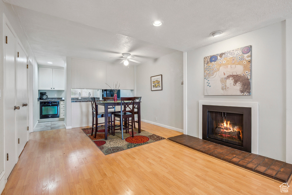 Dining area featuring a warm lit fireplace, light wood-style flooring, baseboards, ceiling fan, and recessed lighting