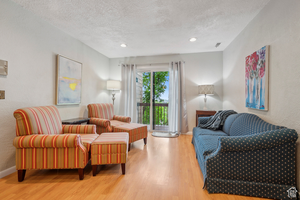 Living area featuring wood finished floors, a textured ceiling, baseboards, a textured wall, and recessed lighting