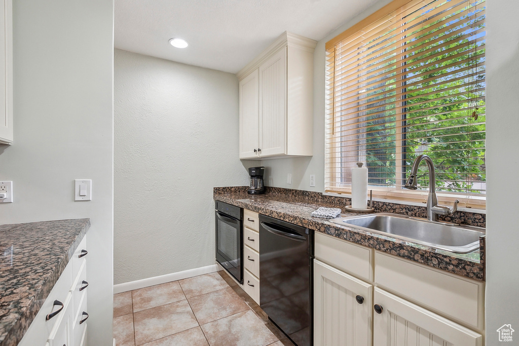 Kitchen featuring black appliances, a sink, dark countertops, light tile patterned floors, and baseboards